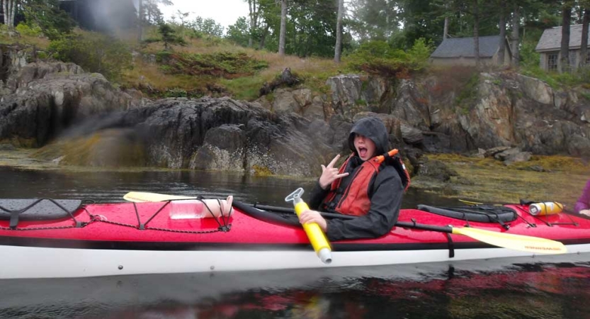 A person sitting inside a red kayaking gives the rock hand symbol. 